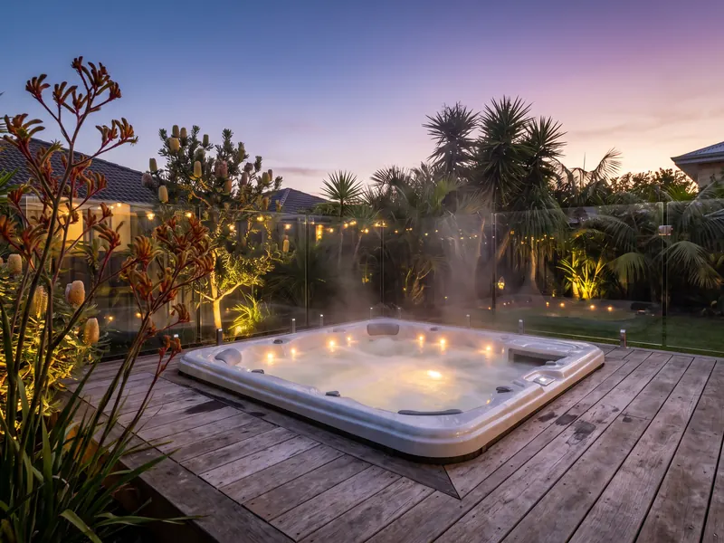 Outdoor spa on a timber deck with a glass safety barrier at dusk